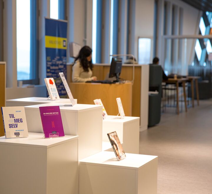 Bokhyller i et bibliotek og en student som leser i en bok