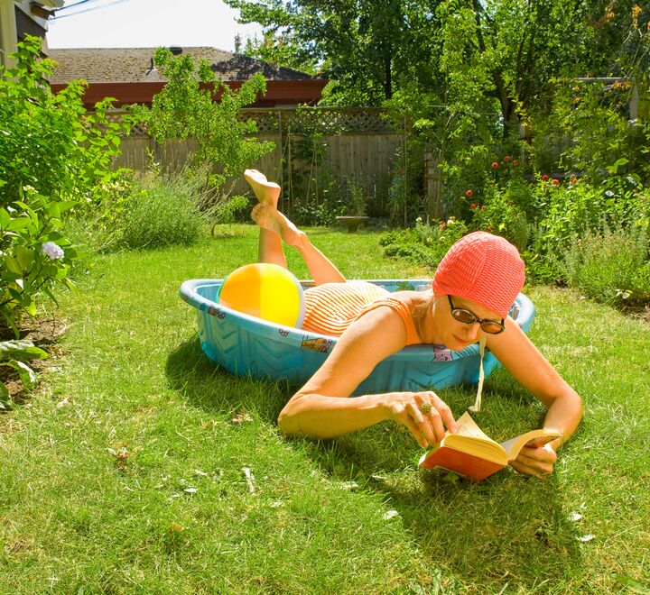 Woman laying in a kids pool reading a book