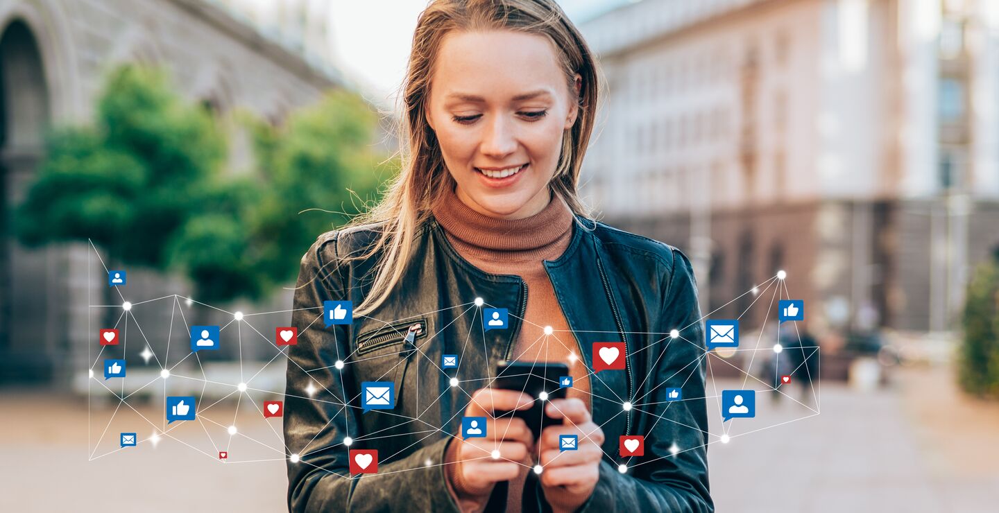 Kvinne står på en plass og holder mobiltelefon.  Rundt telefonen vises likes og emoticons