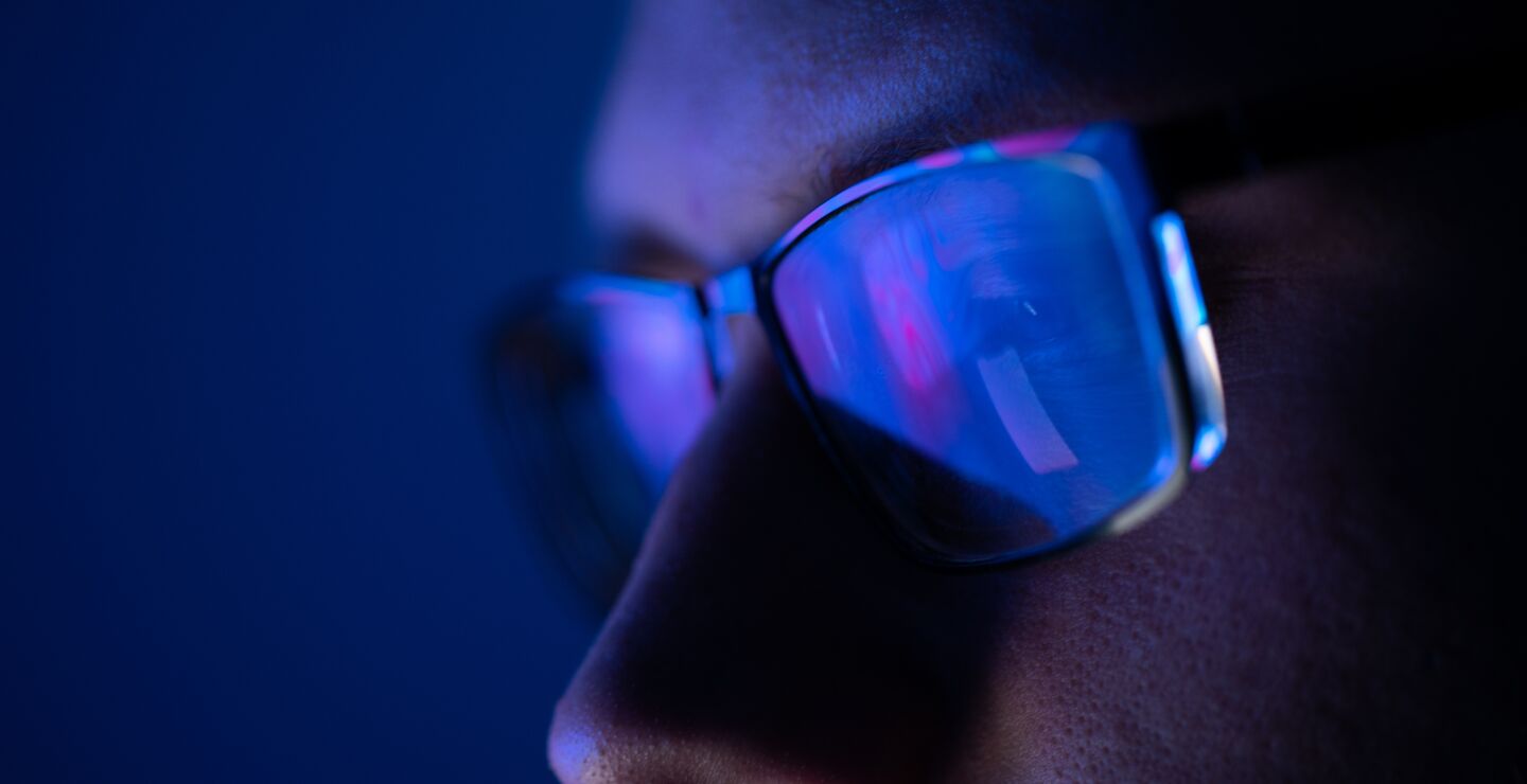 Close-up of a part of a male human face with glasses in neon light.