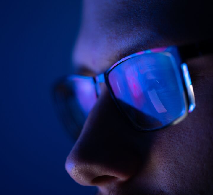 Close-up of a part of a male human face with glasses in neon light.