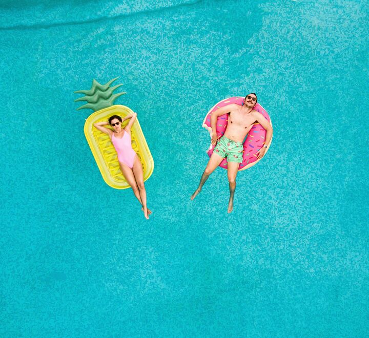 En jente og en gutt som ligger på hver sin bademadrass i et basseng.