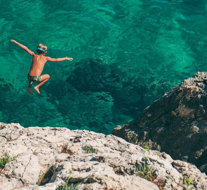 Bilde av gutt som stuper i grønt vann. (Foto: Nikola Radojcic, Unsplash.com).