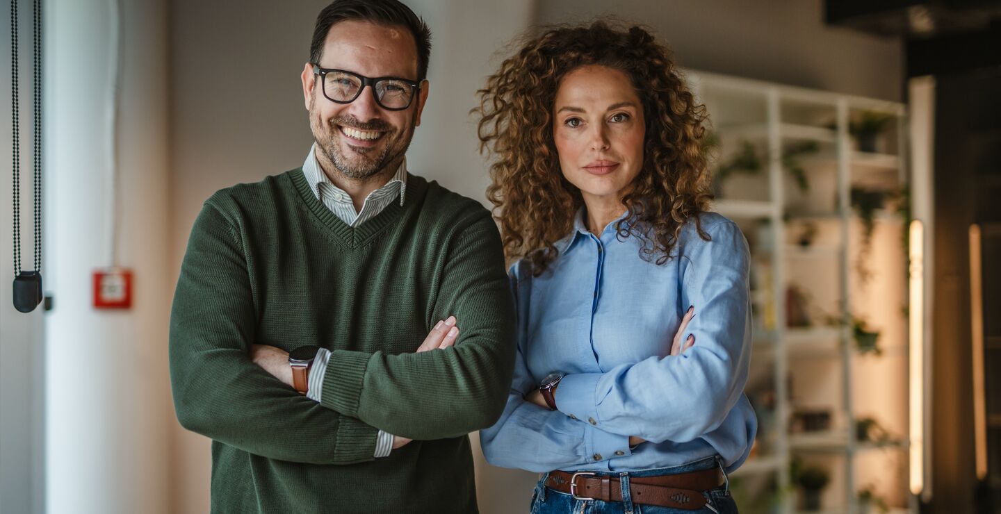 To kolleger står med armene i kors i en moderne kontorsetting.