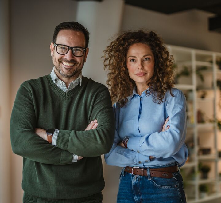 To kolleger står med armene i kors i en moderne kontorsetting.