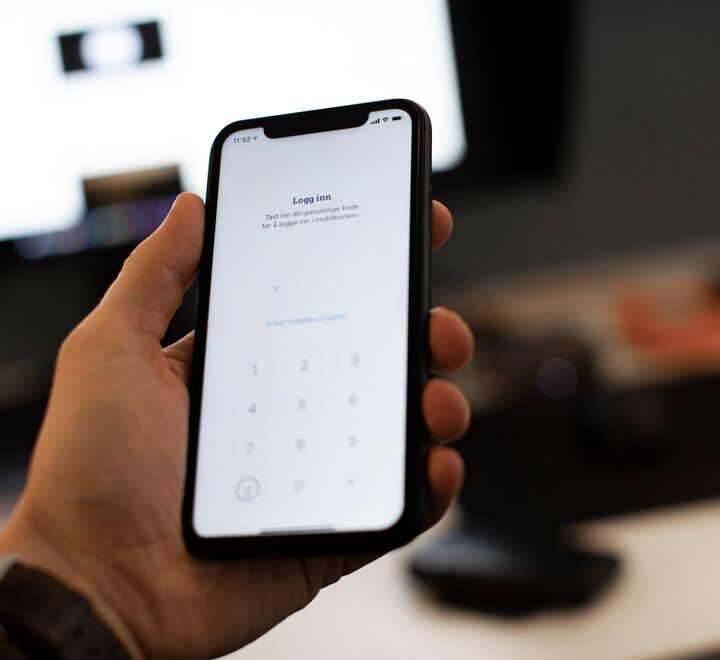 Mann som holder telefon med bank-app foran PC-skjerm