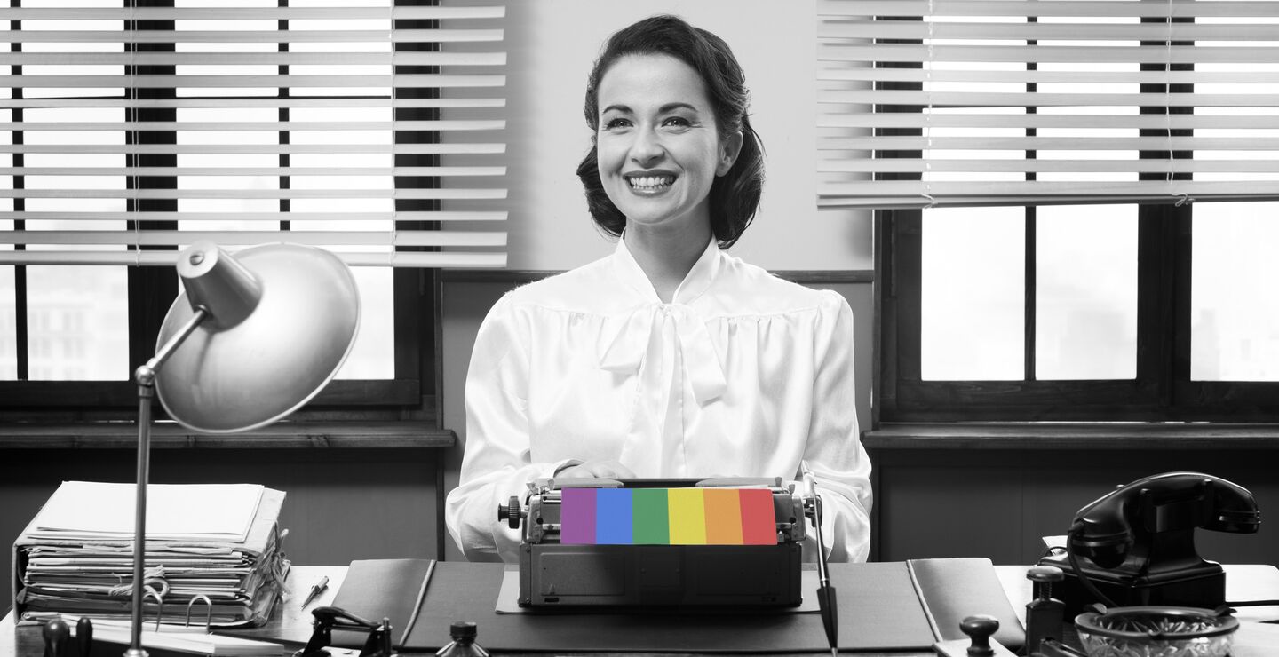 Black and white image of female office worker with rainbow coloured paper coming out of her typewriter