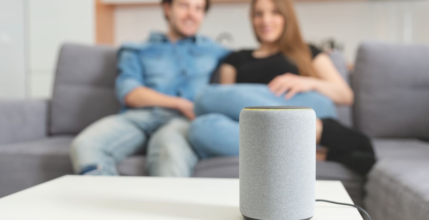 Smart høyttaler i fokus foran to mennesker i sofa