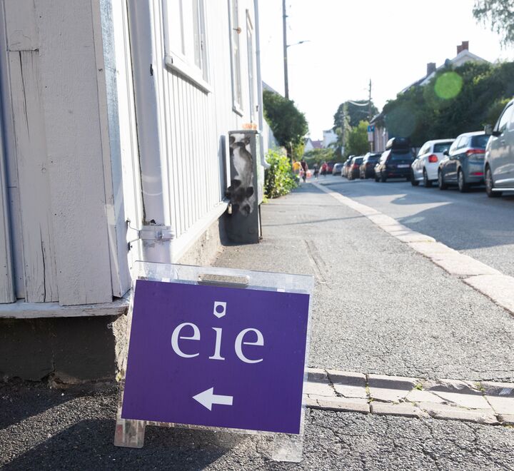Et visnings-skilt som står en gate foran et hvitt hus
