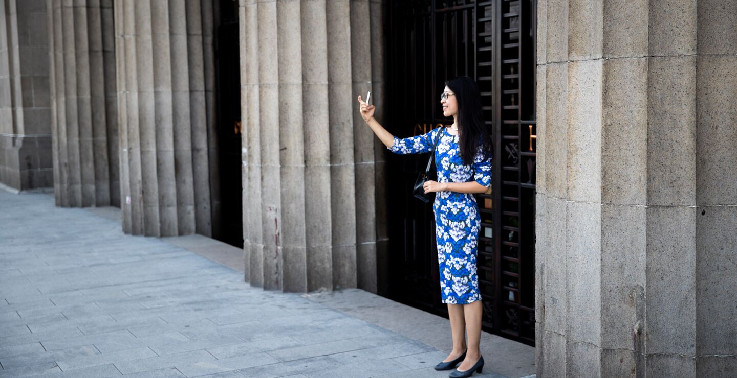 Kinesisk jente med mobil foran en bygning i Shanghai