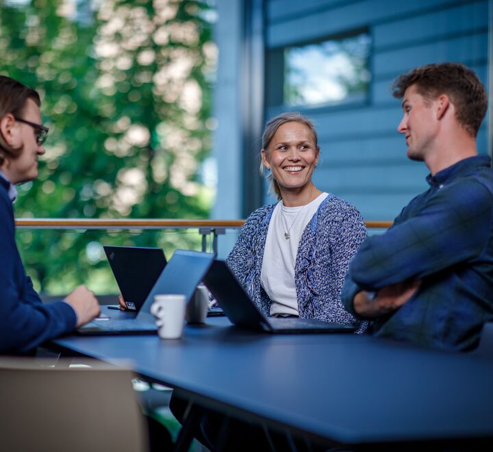 Tre personer som snakker sammen rundt et bord.