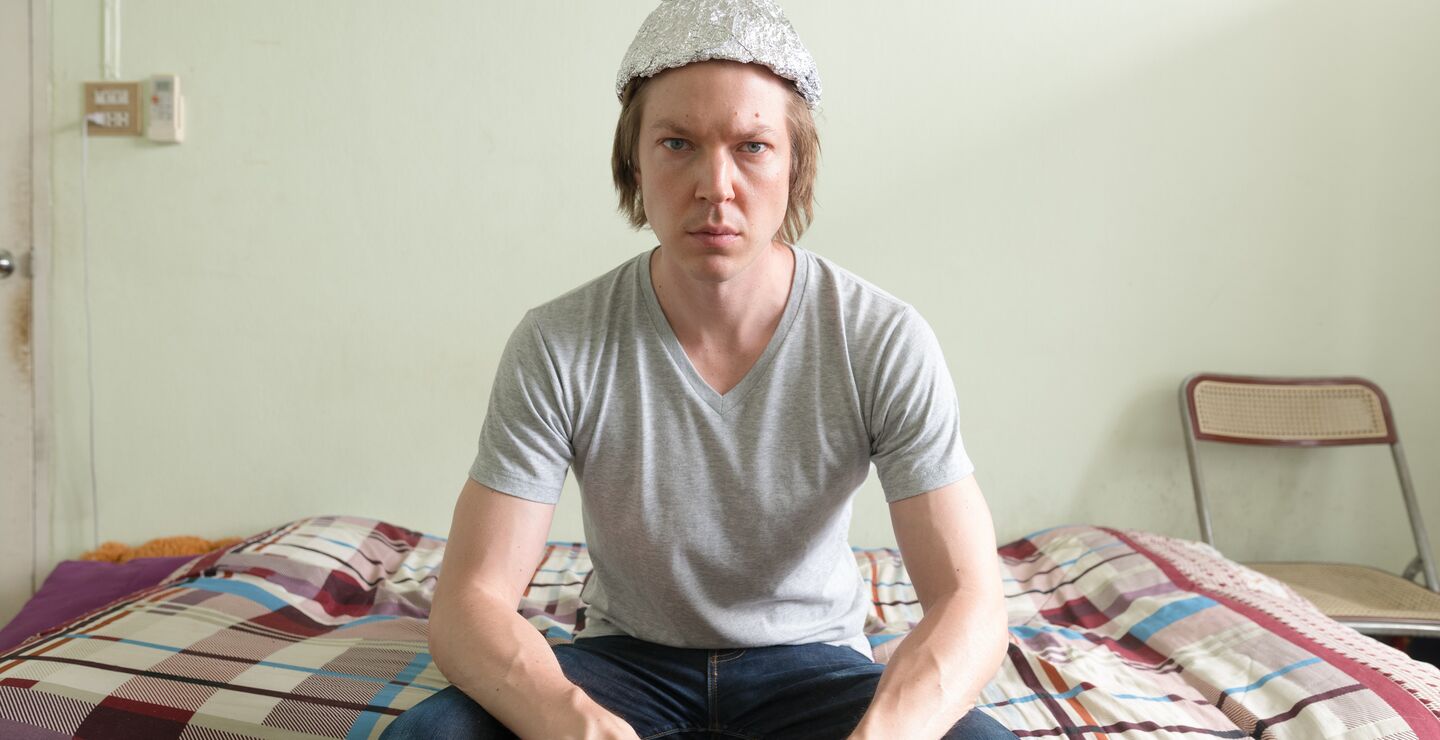 Young man on bed wearing tin foil hat