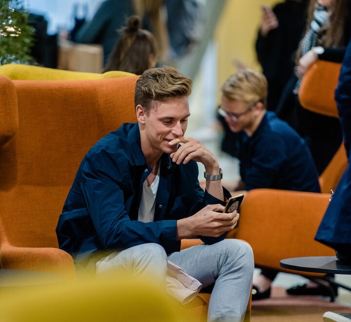 En student som sitter å smiler ned mot mobilen