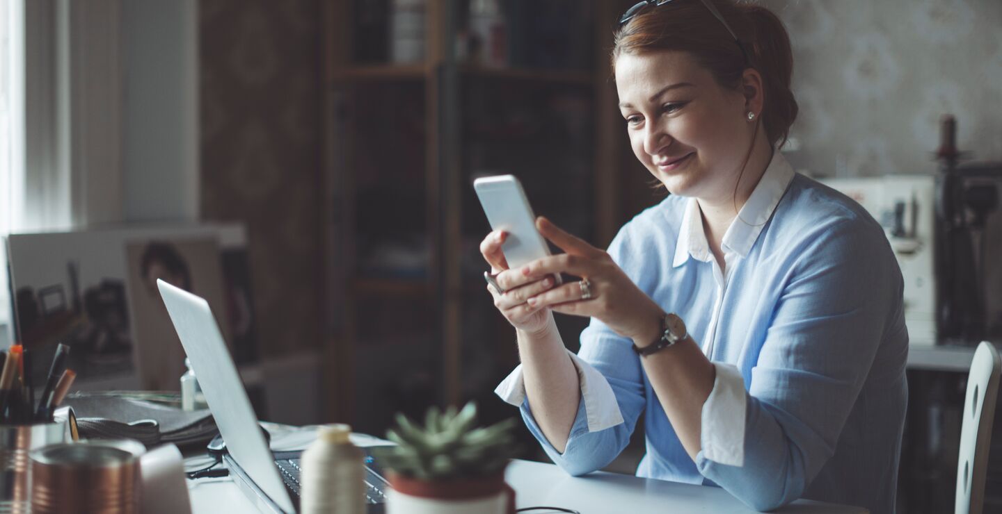 Woman working from her desk at home, using her phone.