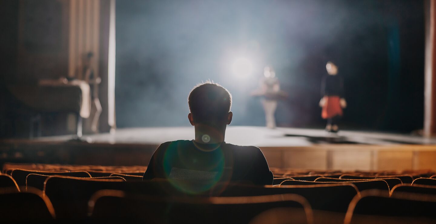 Man sitting in a theatre looking at bright stage