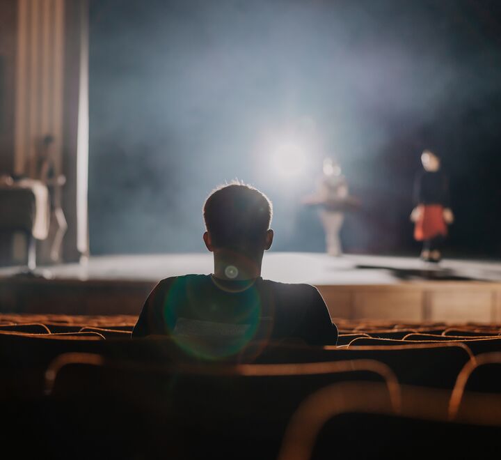 Man sitting in a theatre looking at bright stage