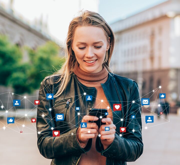 Kvinne står på en plass og holder mobiltelefon.  Rundt telefonen vises likes og emoticons