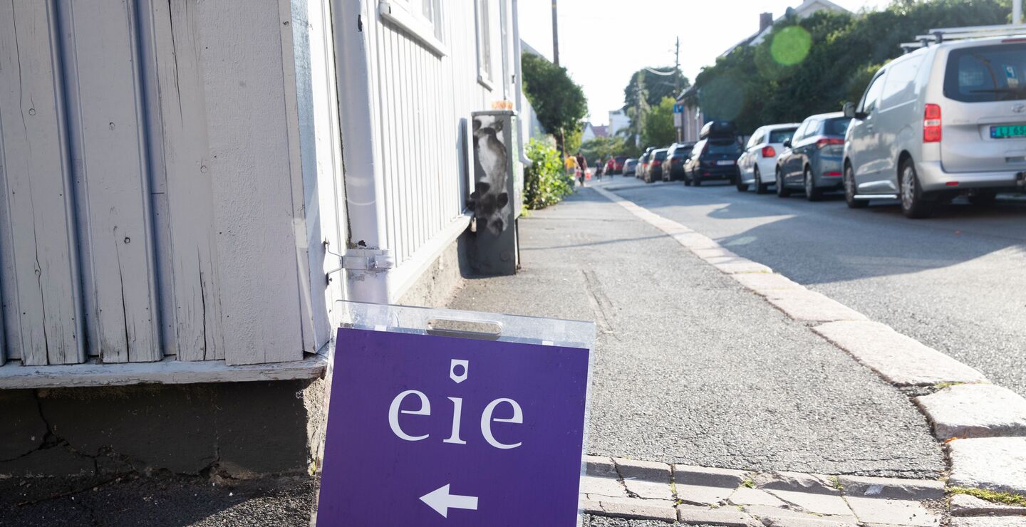 Et visnings-skilt som står en gate foran et hvitt hus