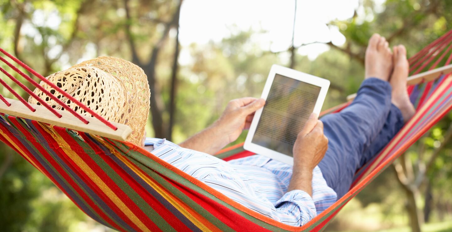 Man wearing a hat relaxing in hammock with E-book