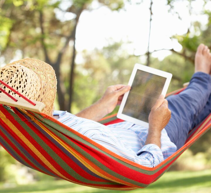 Mann i hatt leser bok i hengekøye