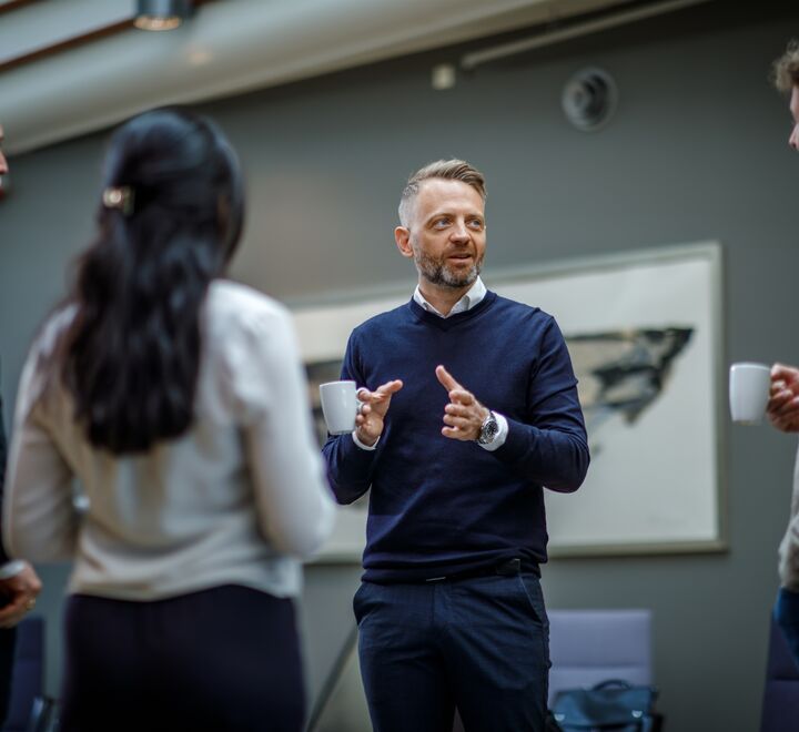 Tre menn og en dame som står og snakker sammen. Fokus på en mann som har ordet.