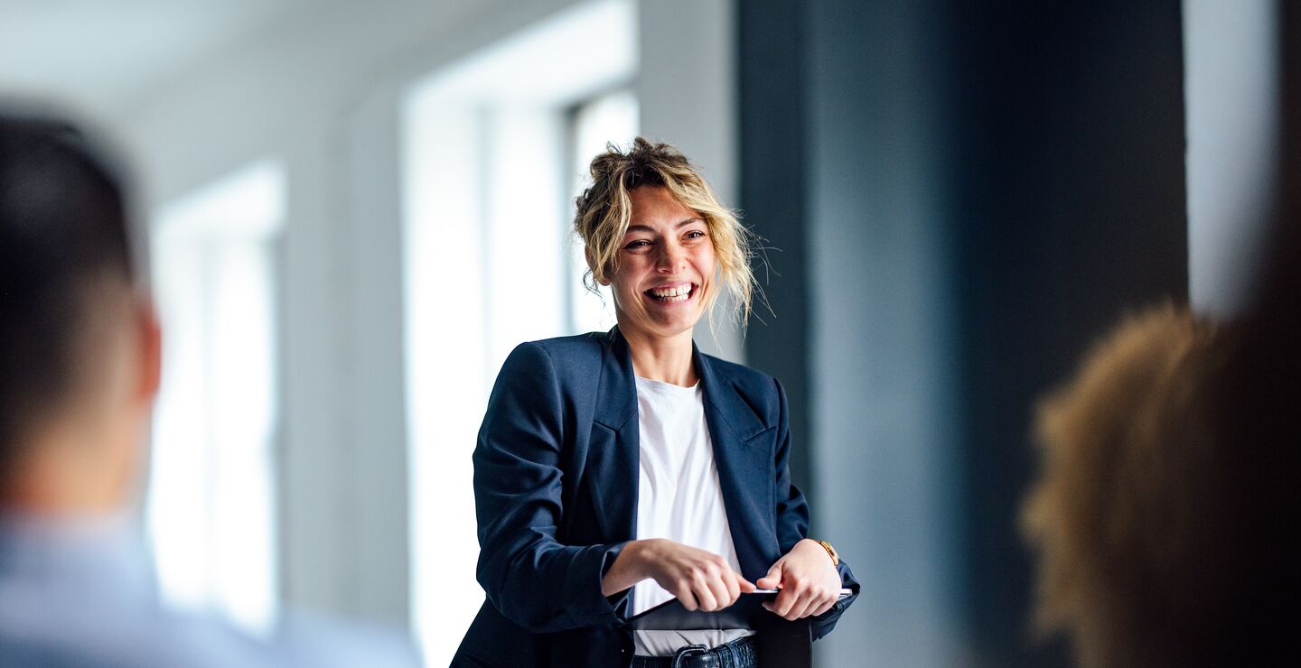 Kvinnelig kollega smiler og holder en presentasjon for sine kolleger.