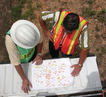To mennesker med hjelm ser og peker på dokumenter