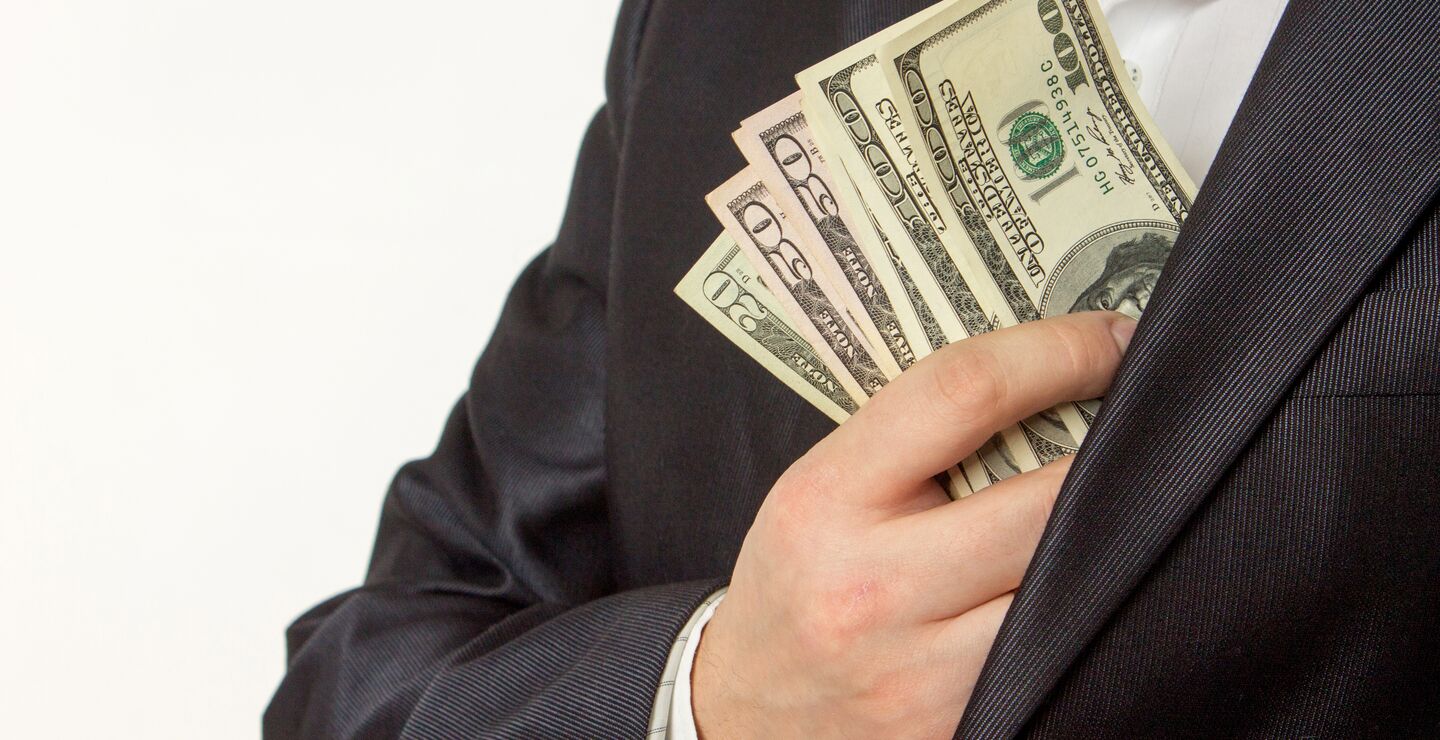 Bilde av en mann i dress som putter penger i jakkelommen