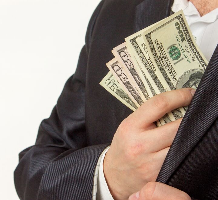 Bilde av en mann i dress som putter penger i jakkelommen