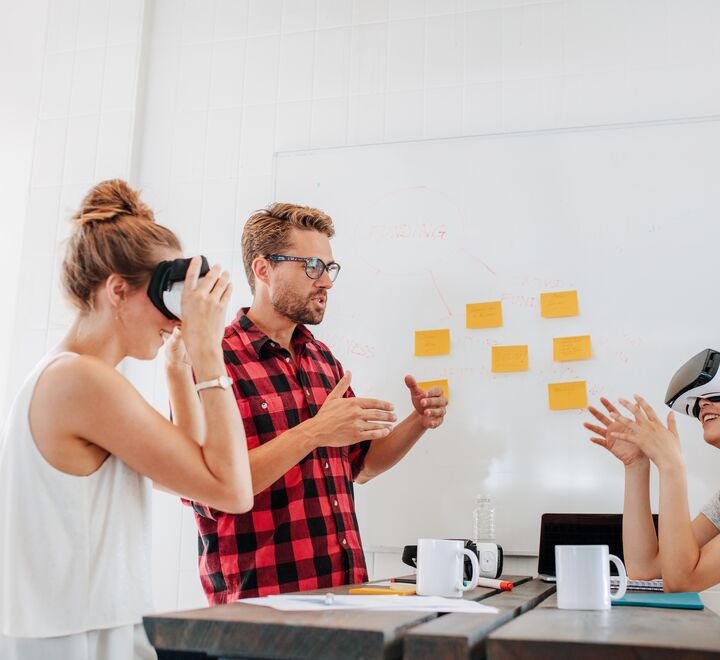 En mann som snakker under et møte, ved siden av en dame som prøver vr-briller