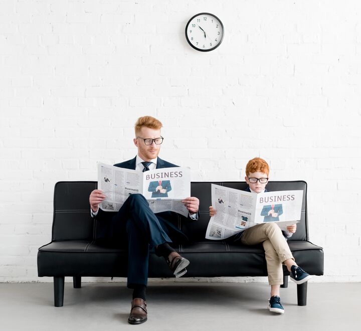Father and son in suits reading newspaper with the headline "Business"
