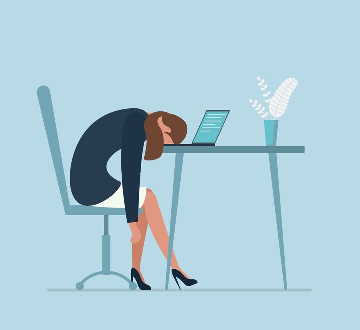 En sliten og stresset kvinne på kontoret ligger med hodet ned i laptopen.