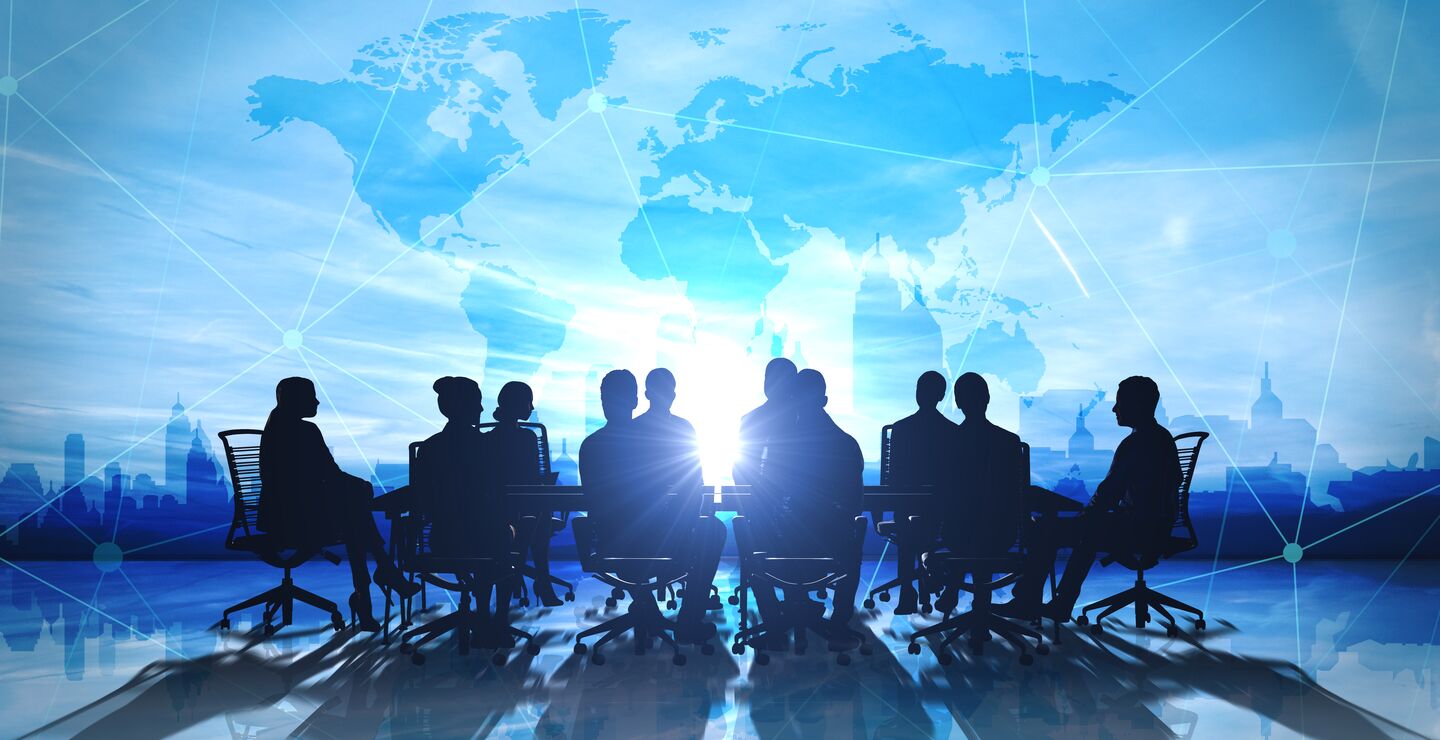 Siluetter rundt et bord, med kart over verden bak