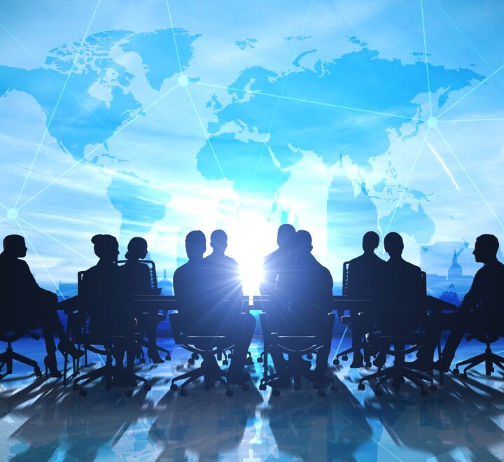 Siluetter rundt et bord, med kart over verden bak