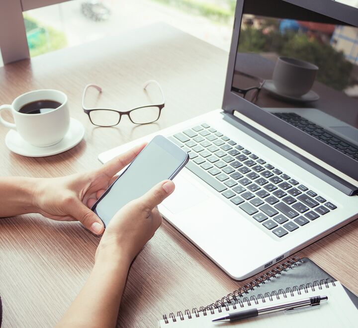 En pc, mobiltelefon og et par briller ligger på et bord
