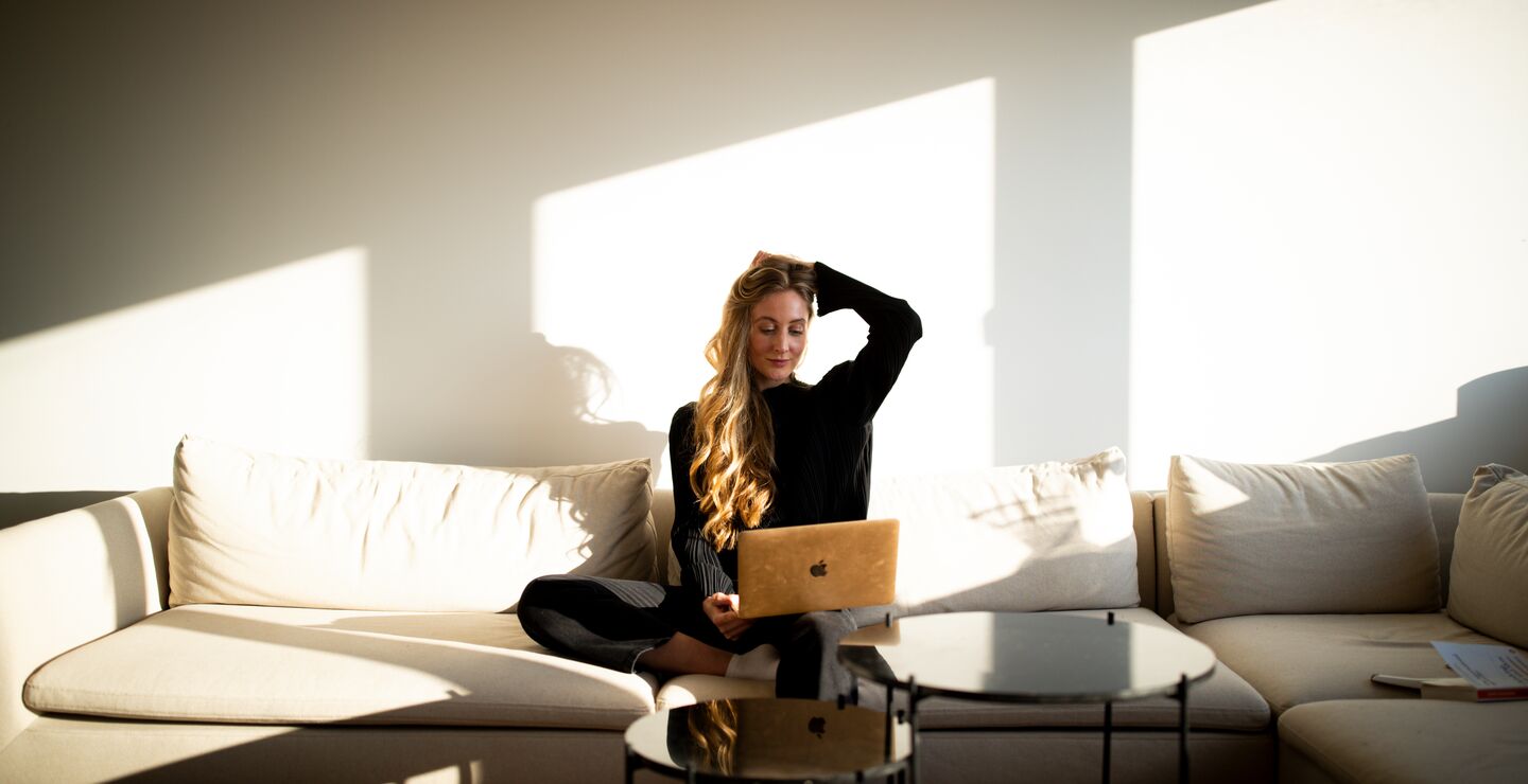 Rita Haugeland som sitter p&aring; en sofa og ser p&aring; pc-en sin