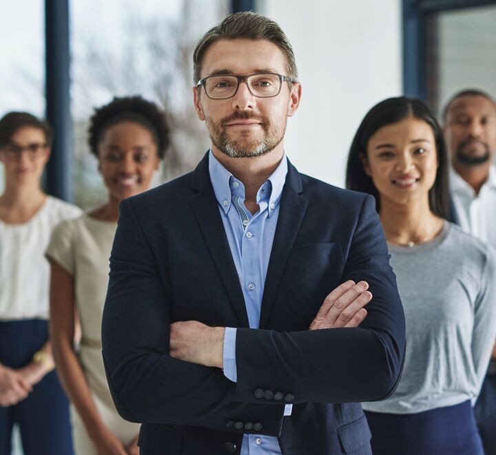 Mann som står med armene i kryss med ansatte stående bak seg