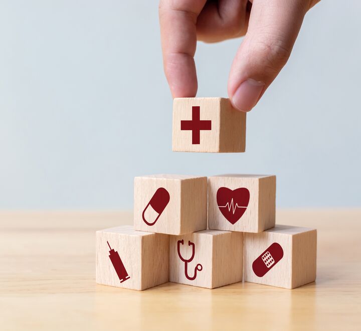 En hånd som plasserer brikker med forskjellige symboler som et hjerte, plaster, en pille og et kryss.