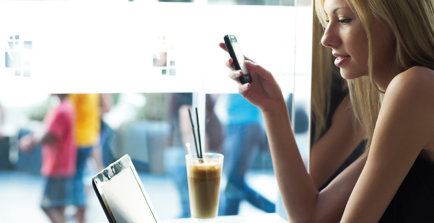 Kvinne med mobil i hånden foran en PC