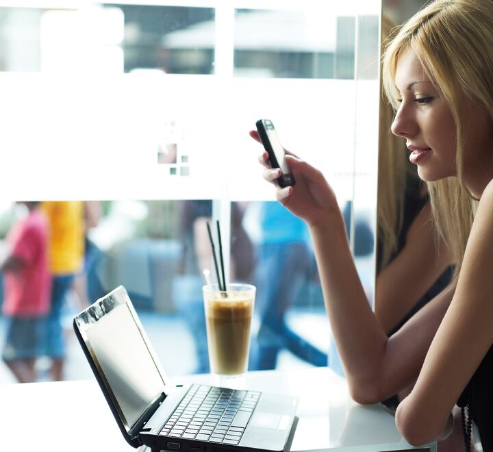 Kvinne med mobil i hånden foran en PC