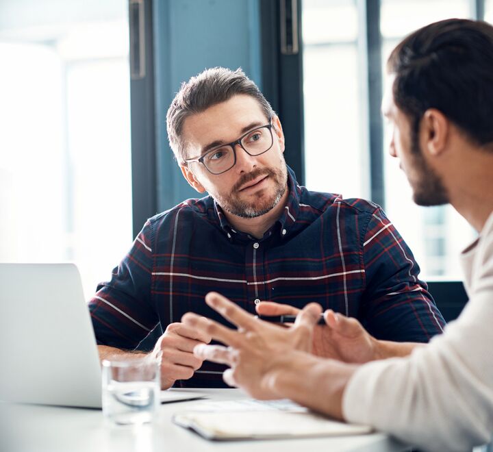 To mannlige kolleger som sitter og snakker sammen foran en laptop