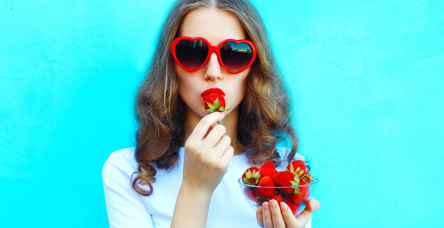 A woman with sunglasses eating a strawberry.