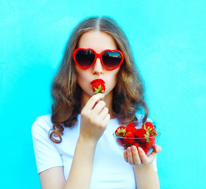 A woman with sunglasses eating a strawberry.