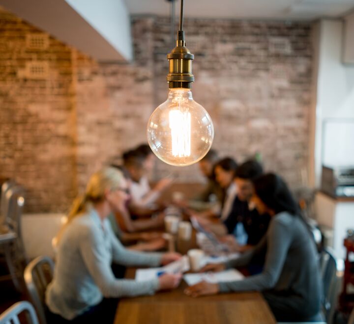 Gruppe med mennesker som sitter og jobber sammen. En lyspære i fokus.