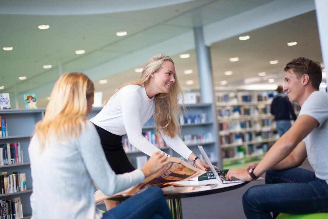 Student som lener seg smilende over et bord på biblioteket