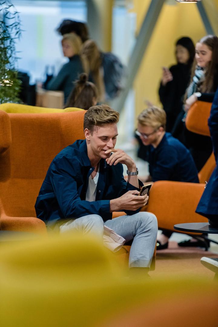 En student som sitter å smiler ned mot mobilen