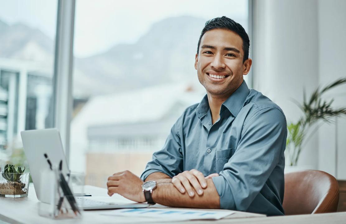 Bilde av en smilende mann som sitter å jobber på en PC.