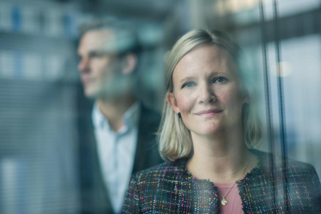 Kvinne ser inn i kamera, mann blurry i bakgrunnen