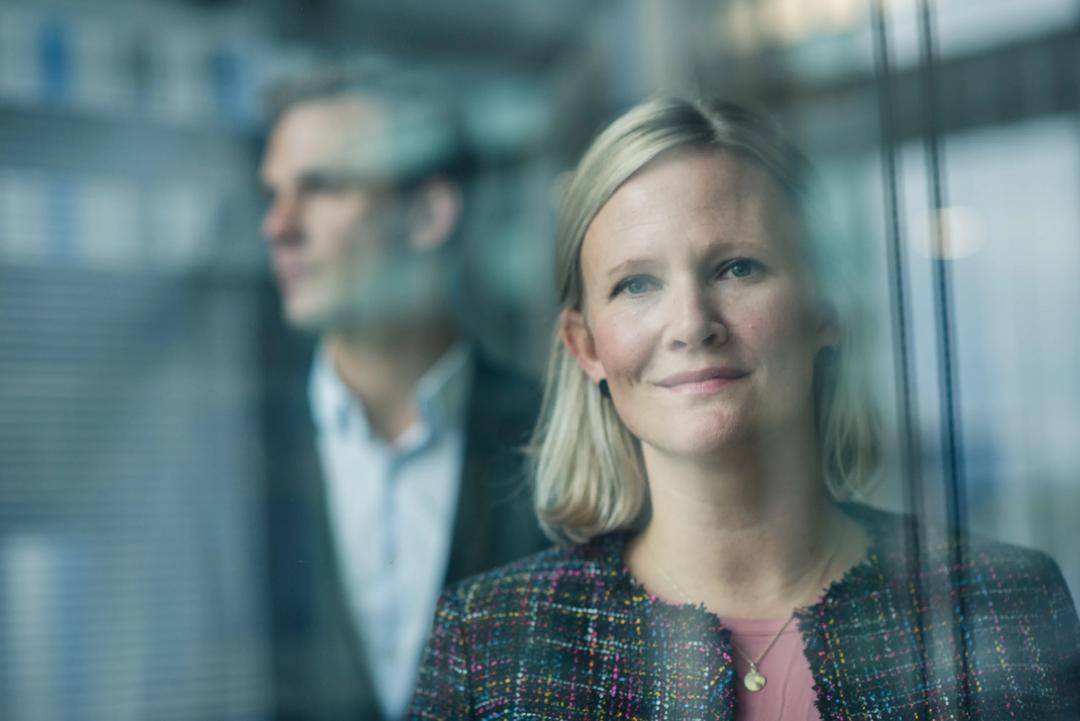 Kvinne ser inn i kamera, mann blurry i bakgrunnen