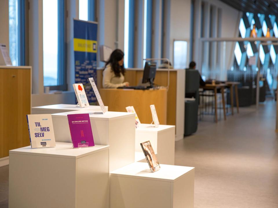 Bokhyller i et bibliotek og en student som leser i en bok